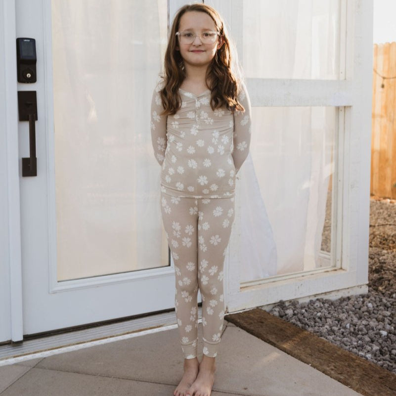 A child standing in front of a door, wearing beige bamboo two-piece pajamas with white polka dots.