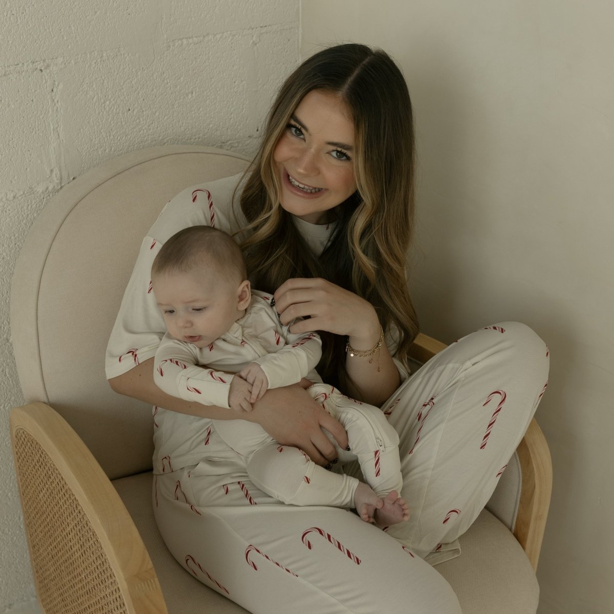 Woman and baby sitting on a chair wearing matching pajamas with candy cane patterns.