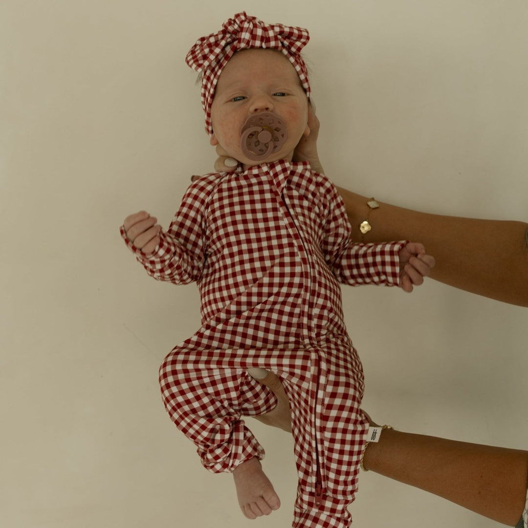 Baby in a red and white checkered outfit with matching headband on a neutral background