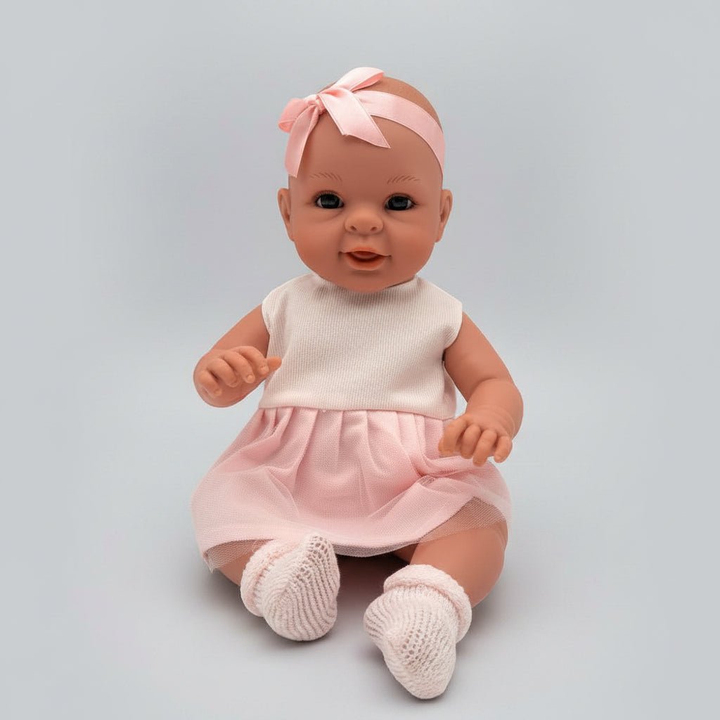 Baby doll in a pink dress and headband sitting on a wooden floor.