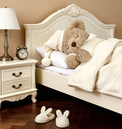 Children's bedroom with a teddy bear on a bed, nightstand with lamp and clock, and slippers on the floor.