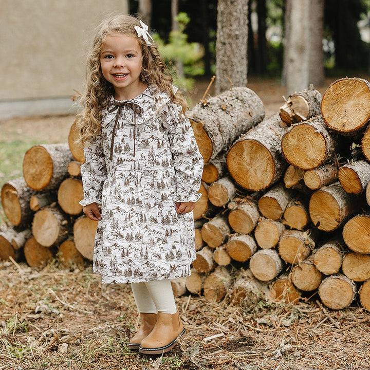 Young girl standing in front of a stack of logs with trees in the background