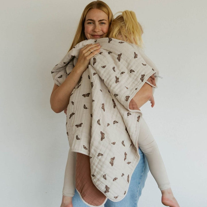 Woman holding a child wrapped in a patterned blanket against a plain background