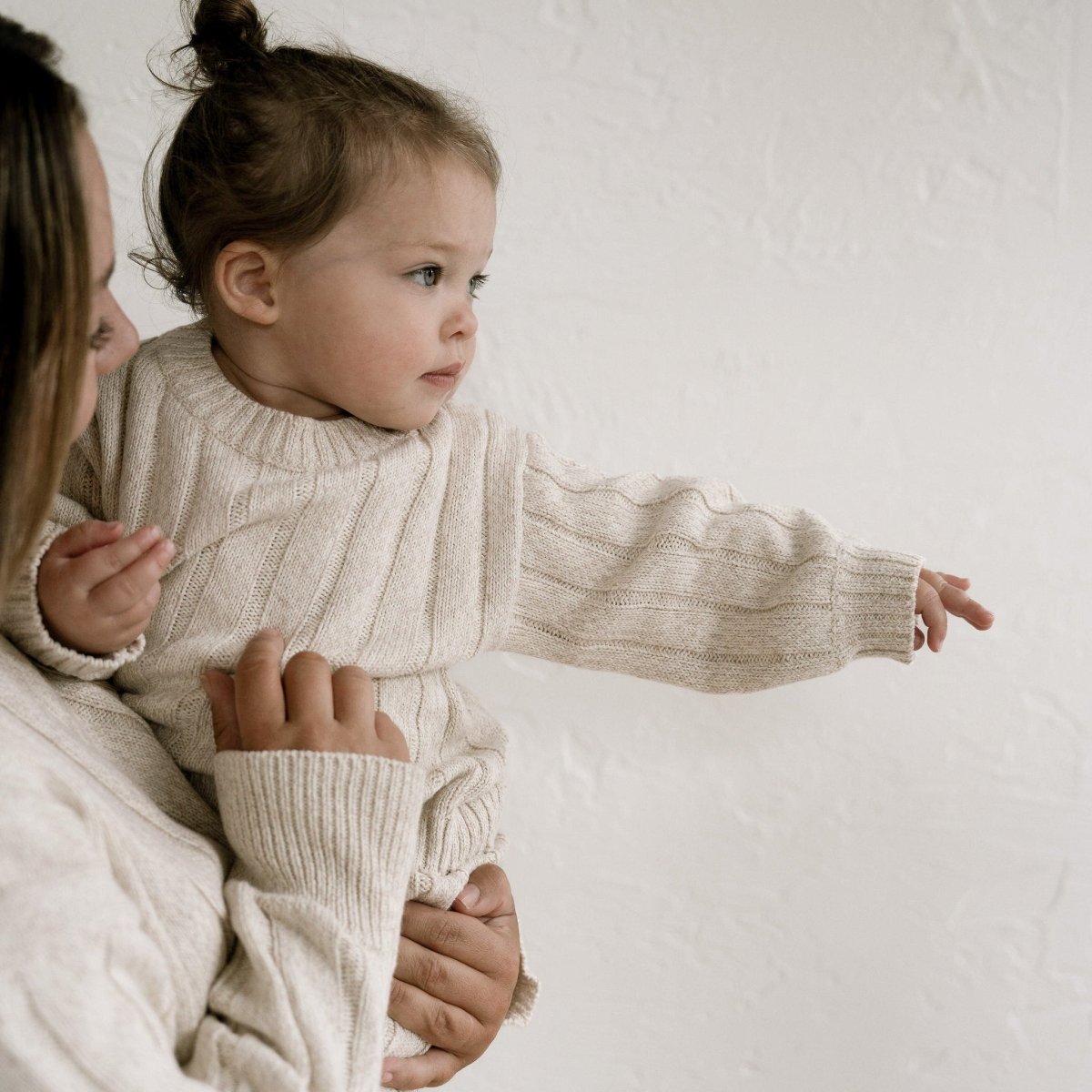 Woman holding a child in a beige sweater against a white background