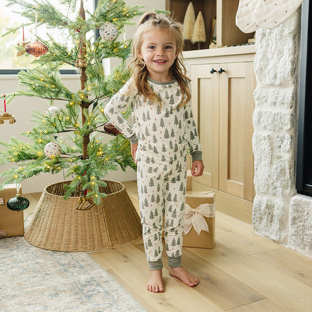 Child in pajamas standing next to a decorated Christmas tree in a cozy living room.
