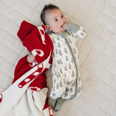 Baby lying on a quilted surface with a red and white patterned blanket and gray onesie.