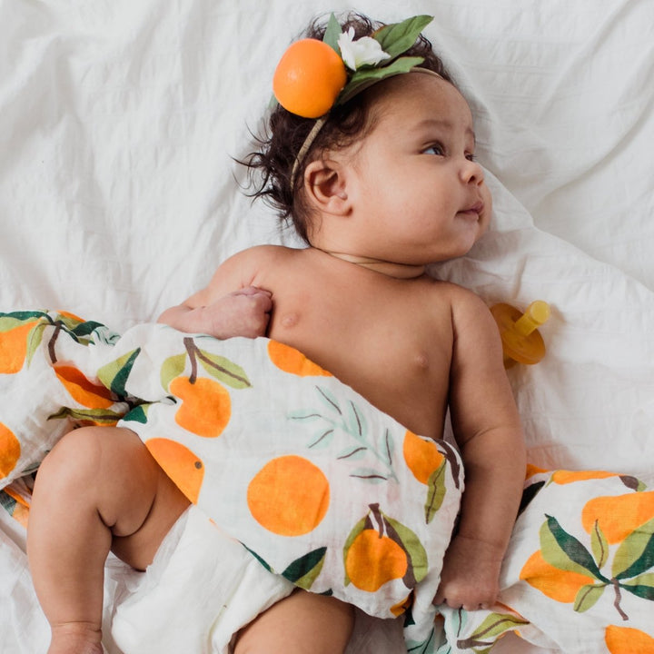 Baby wrapped in a cloth with orange pattern on a white blanket