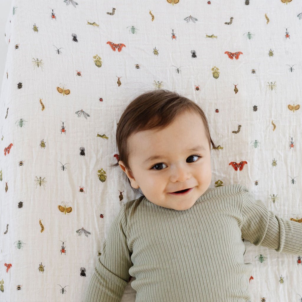 Baby in green ribbed outfit lying on a crib with a patterned sheet