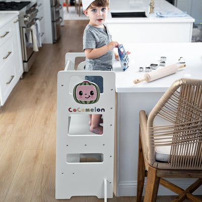 Child in a kitchen wearing a chef's hat and standing on a step stool with a CoComelon logo.