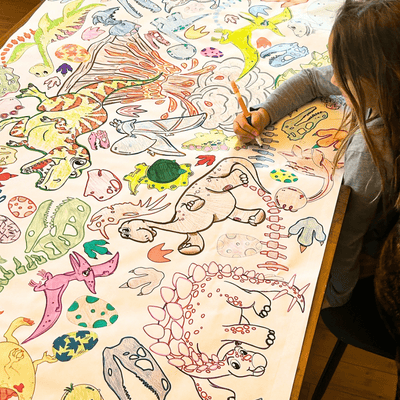 A kid is coloring a large sheet of dinosaur illustrations with crayons.