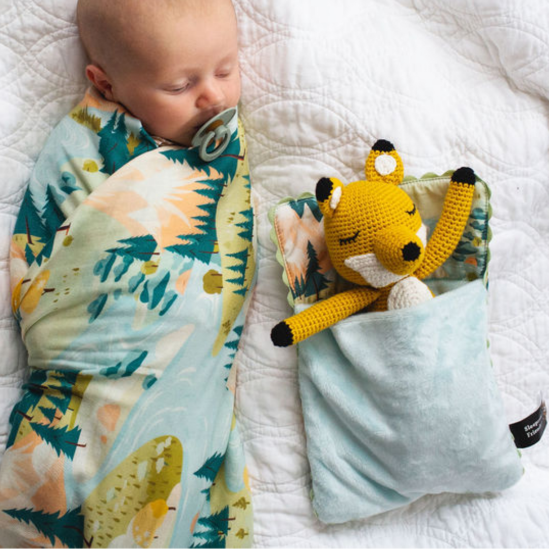 Baby sleeping with a swaddle and toy on a white blanket