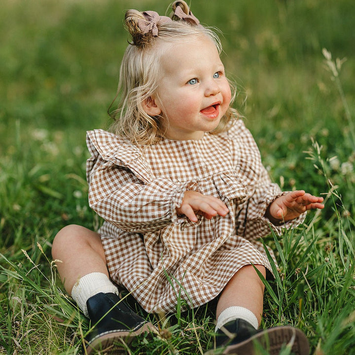 Child in a checkered dress sitting in a grassy field