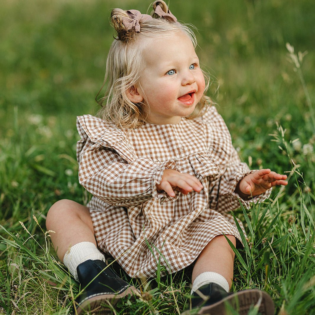Child in a checkered dress sitting in a grassy field