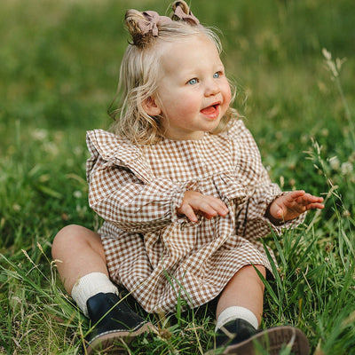 Child in a checkered dress sitting in a grassy field