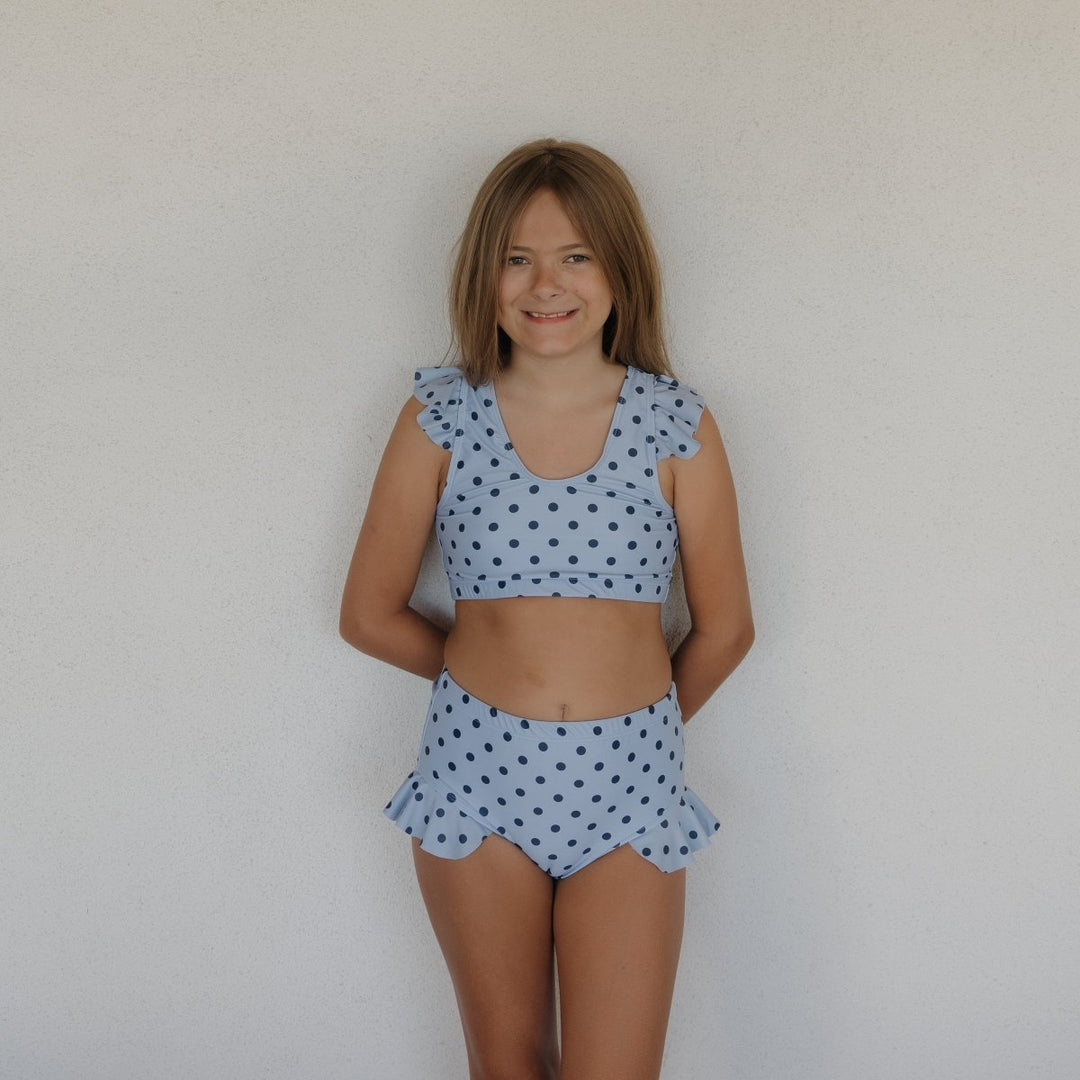 Young girl wearing a light blue polka dot two-piece outfit against a plain background
