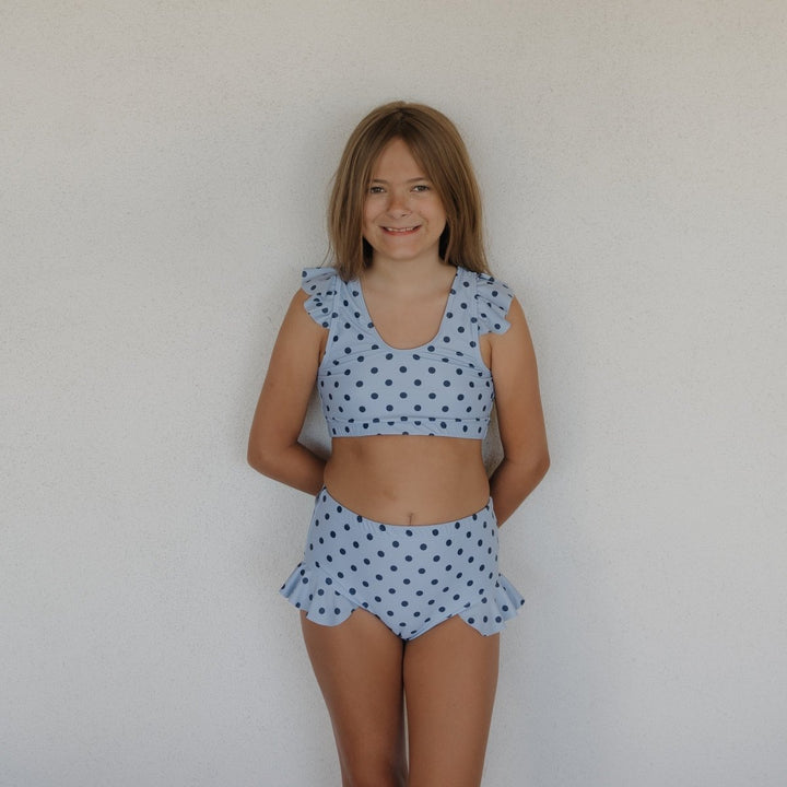 Young girl wearing a light blue polka dot two-piece outfit against a plain background