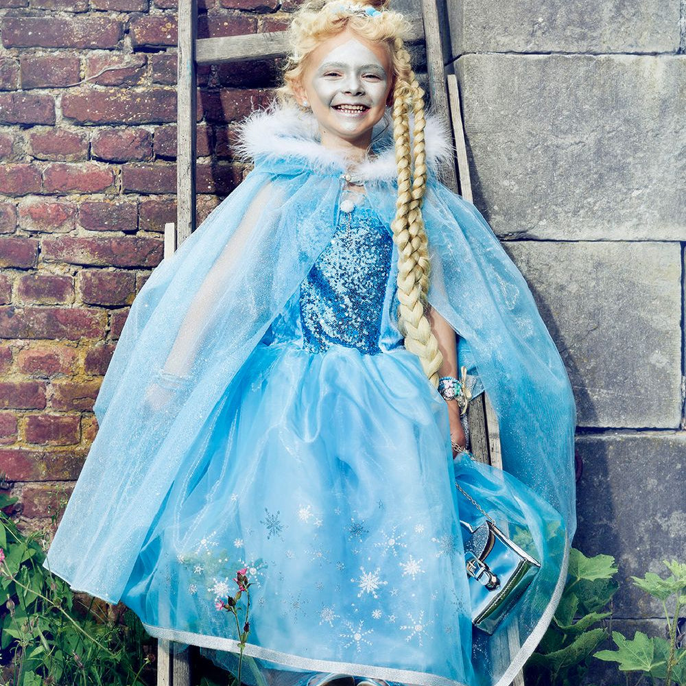 Child in a blue dress with snowflake design against a brick wall.