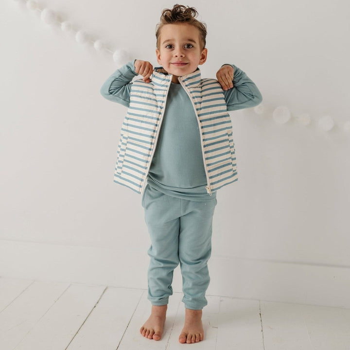 Child wearing a striped shirt and light blue pants against a white background