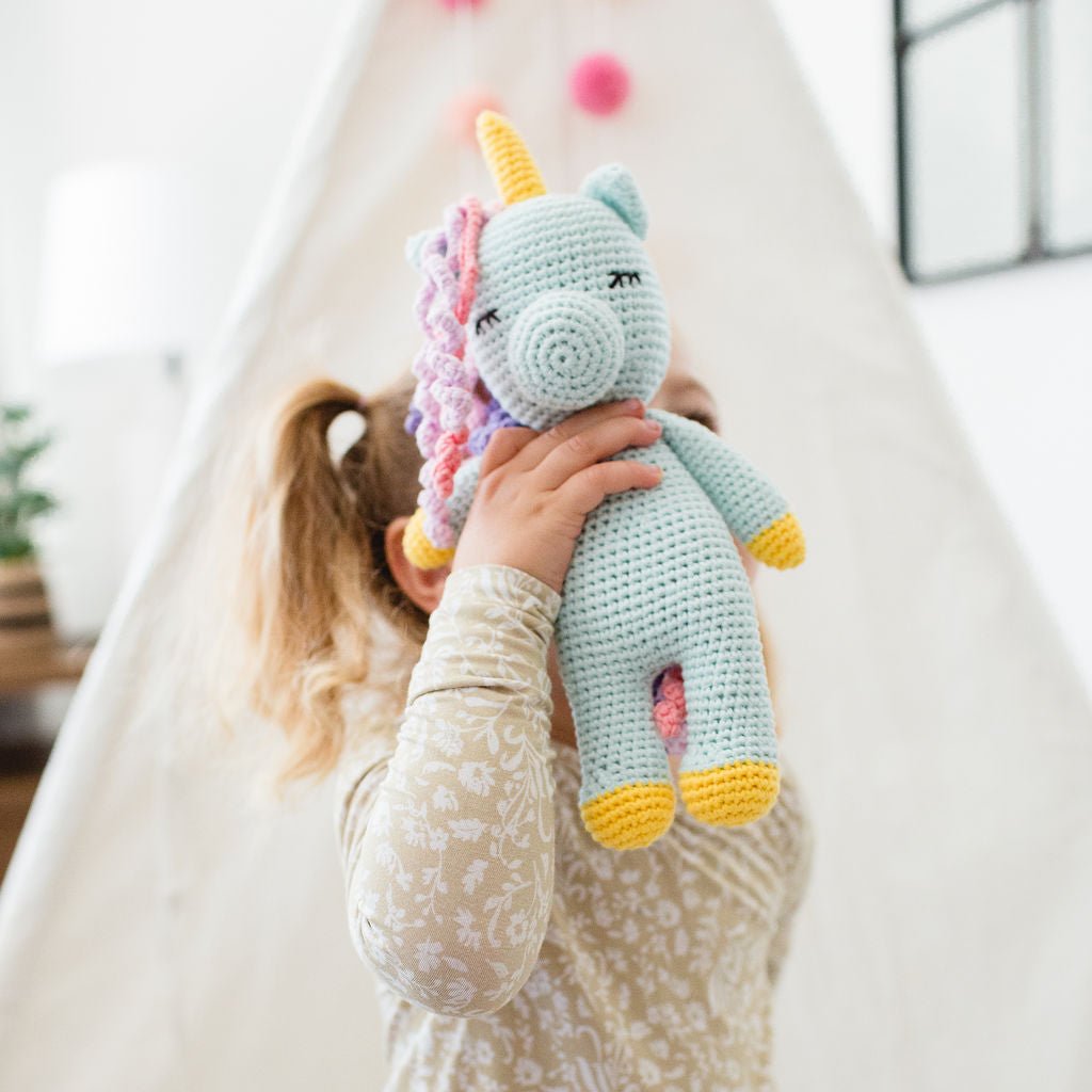 Child holding a crocheted unicorn toy in a cozy indoor setting