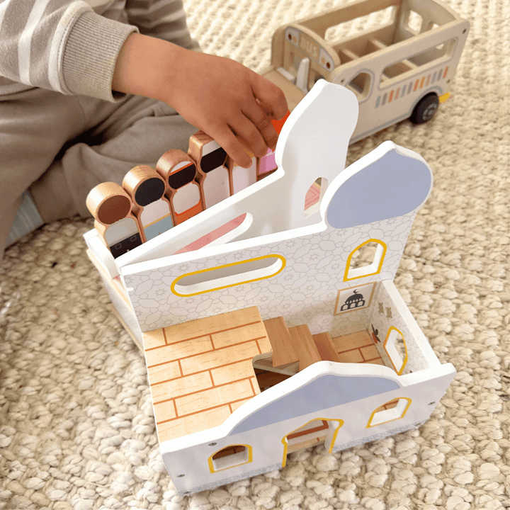 Child playing with a wooden toy house and accessories on a carpeted floor.