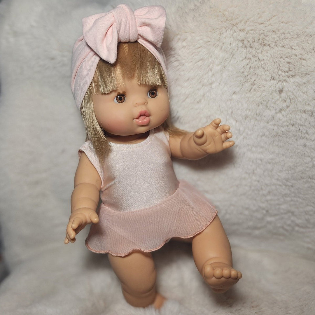 Doll wearing a pink outfit with a bow on a textured surface