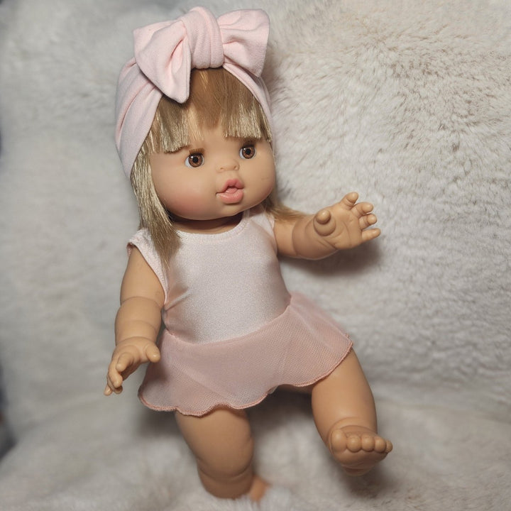 Doll wearing a pink outfit with a bow on a textured surface