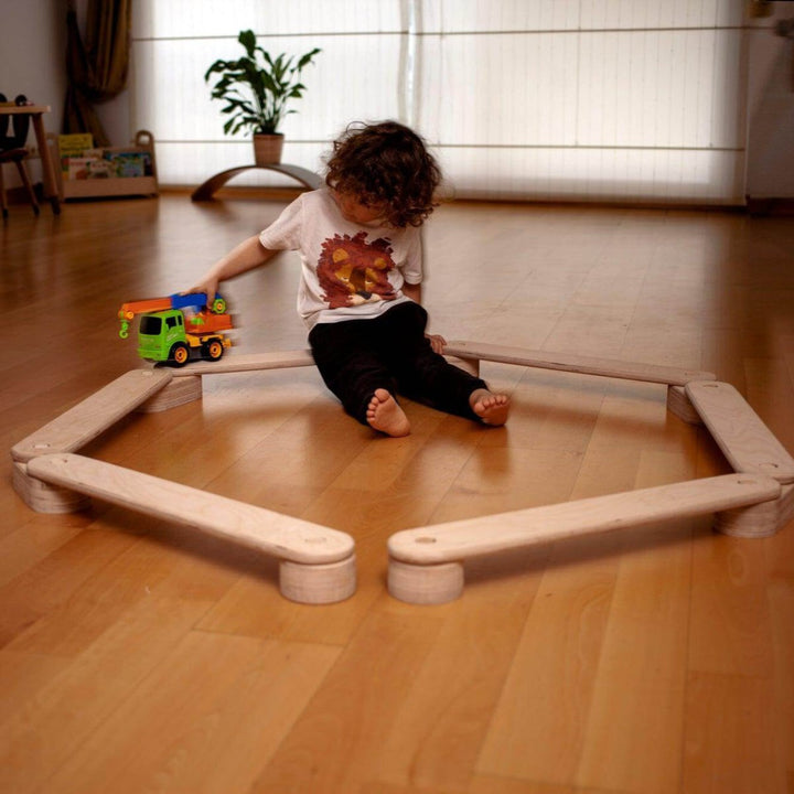 Child playing with a toy truck on a wooden floor in a room with a couch and plant.