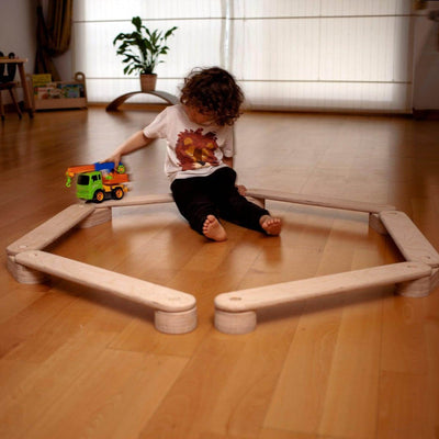 Child playing with a toy truck on a wooden floor in a room with a couch and plant.