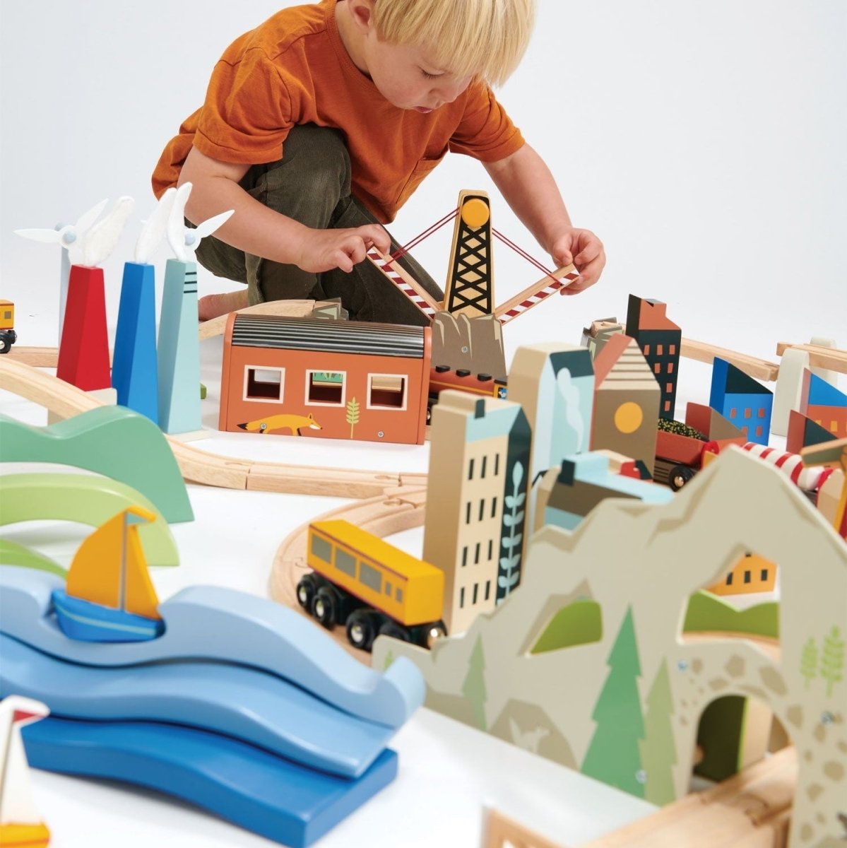 Child playing with a wooden toy train set on a white surface