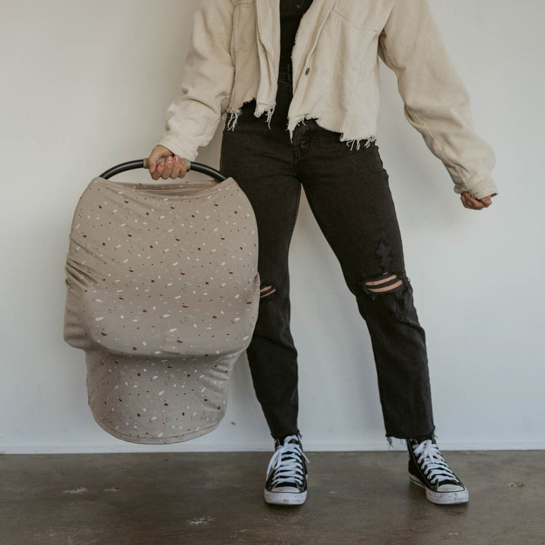 Person holding a beige baby carrier with a white wall background