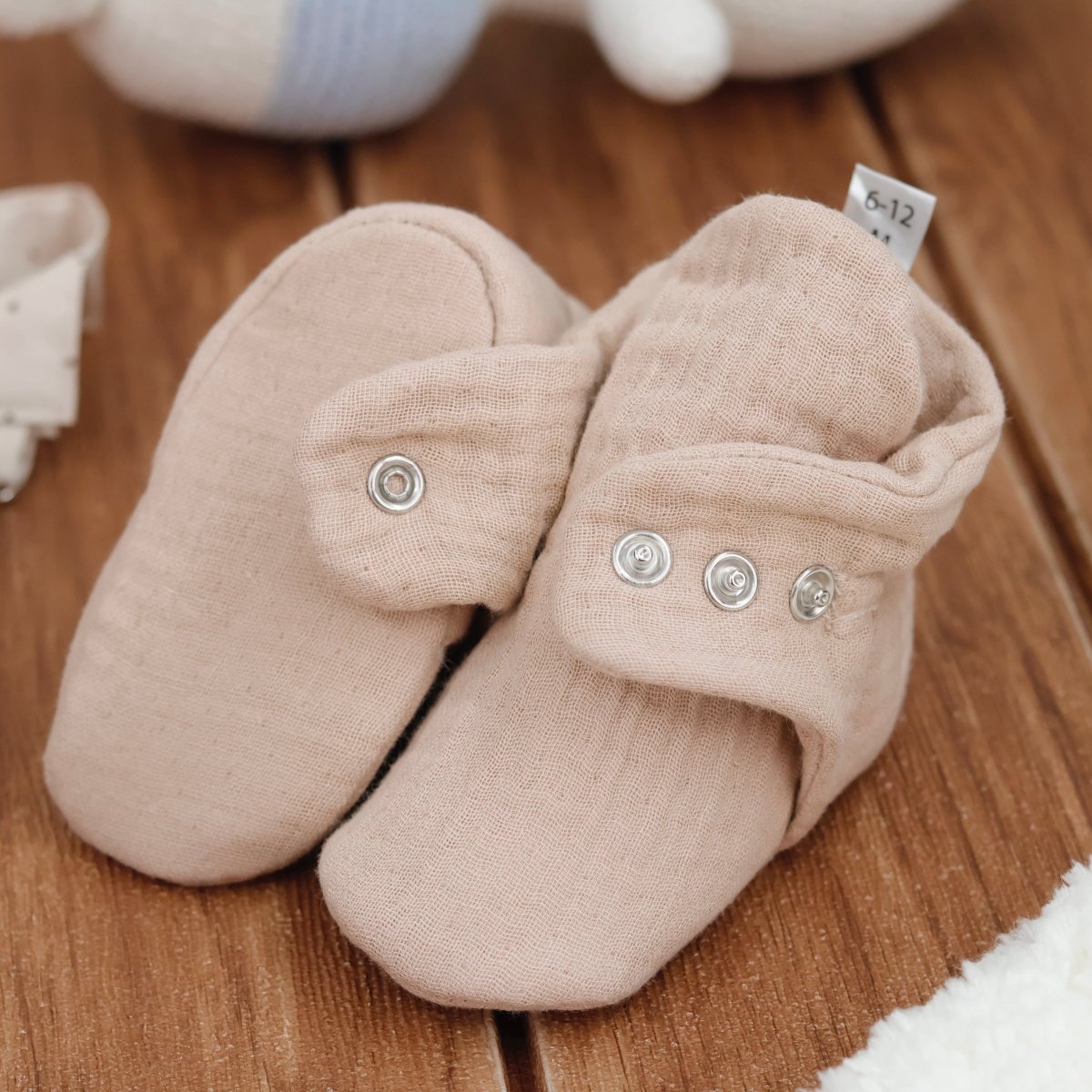 Beige baby booties with button details on a wooden surface