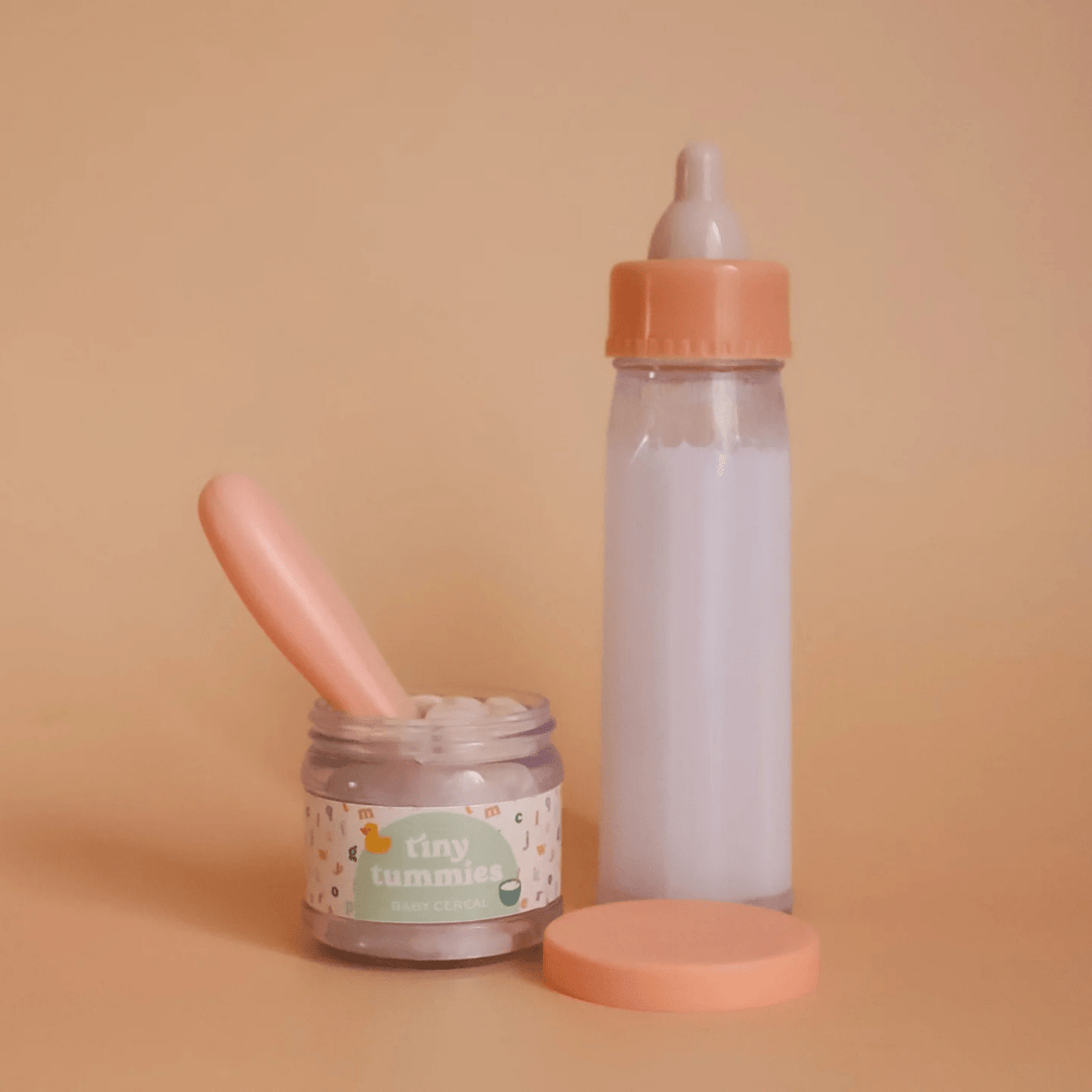 Baby doll bottle, jar, and spoon on a beige background with &