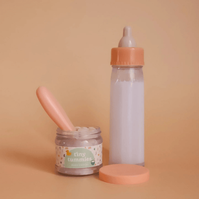 Baby doll bottle, jar, and spoon on a beige background with 'tiny tummies' branding.