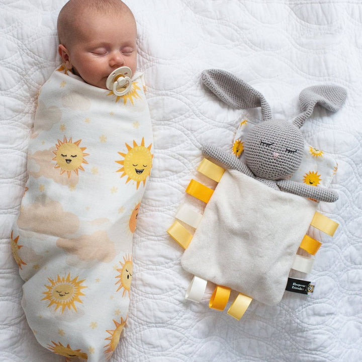 Baby swaddled in a blanket with sun patterns next to a soft toy on a white surface