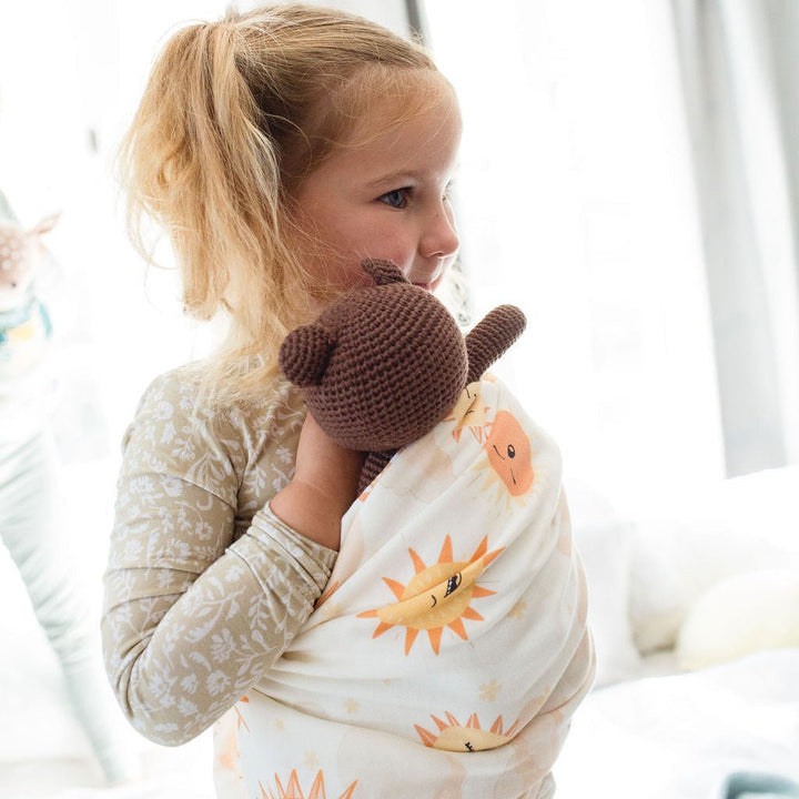 Child wrapped in a swaddle with bear toy, surrounded by soft bedding