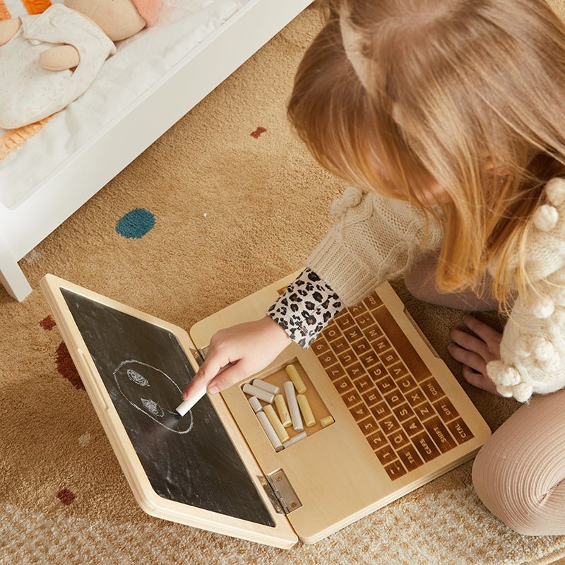 Child playing with a wooden toy laptop on a carpeted floor