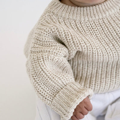 Close-up of a baby wearing a beige knitted sweater on a light background