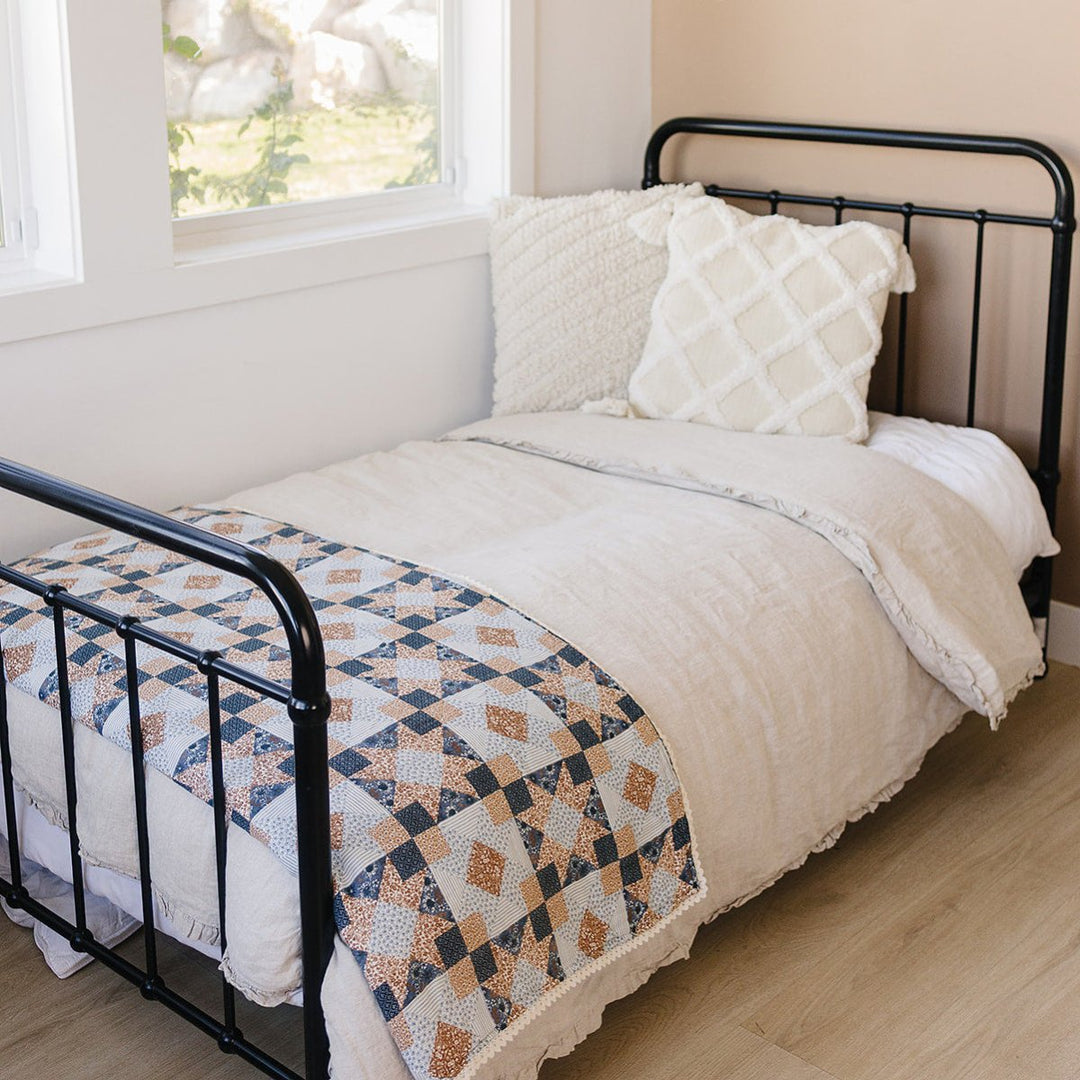 Bedroom with a black metal bed frame, white bedding, and a quilt with geometric pattern.
