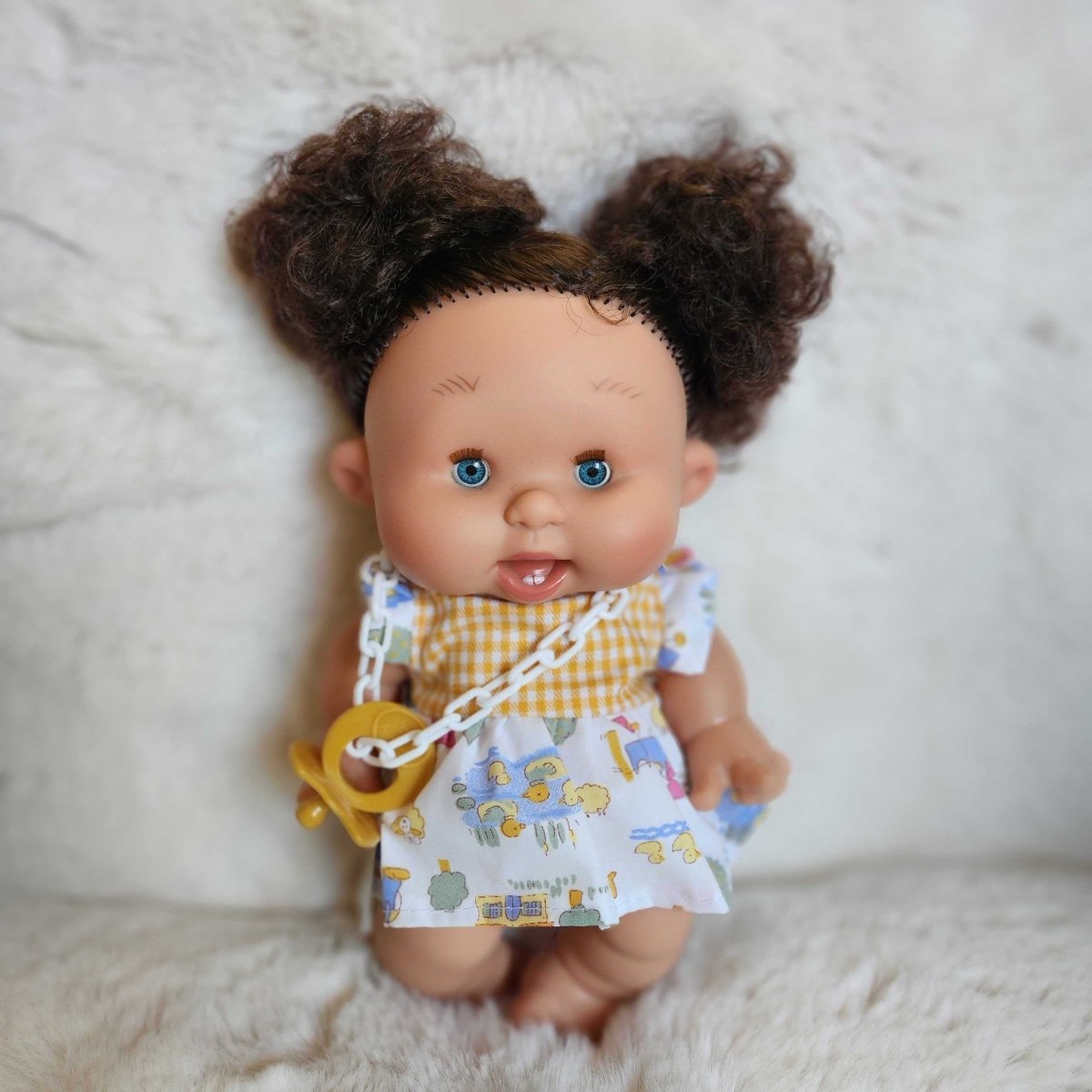 Pepote doll with curly hair wearing a yellow bib and white outfit 