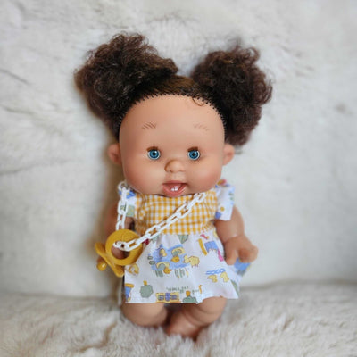 Pepote doll with curly hair wearing a yellow bib and white outfit 