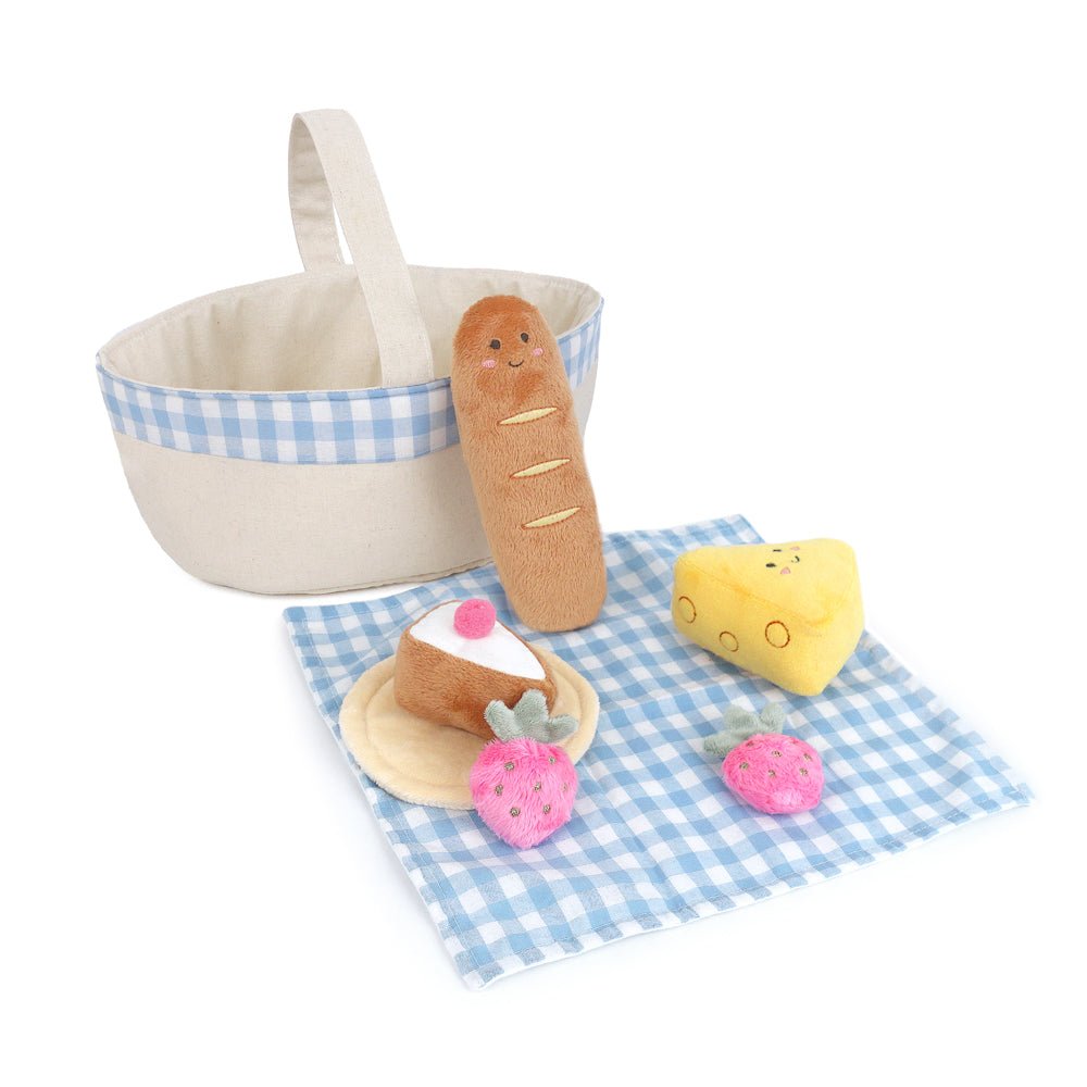 Toy food items including a bread roll, cake, and cheese on a checkered cloth with a basket.