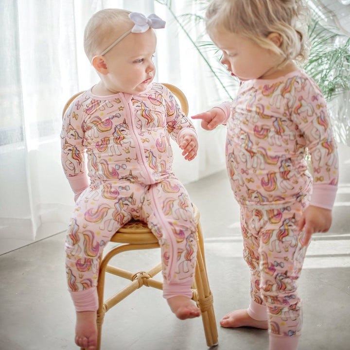 Two children wearing pink pajamas with unicorn patterns in a bright room.