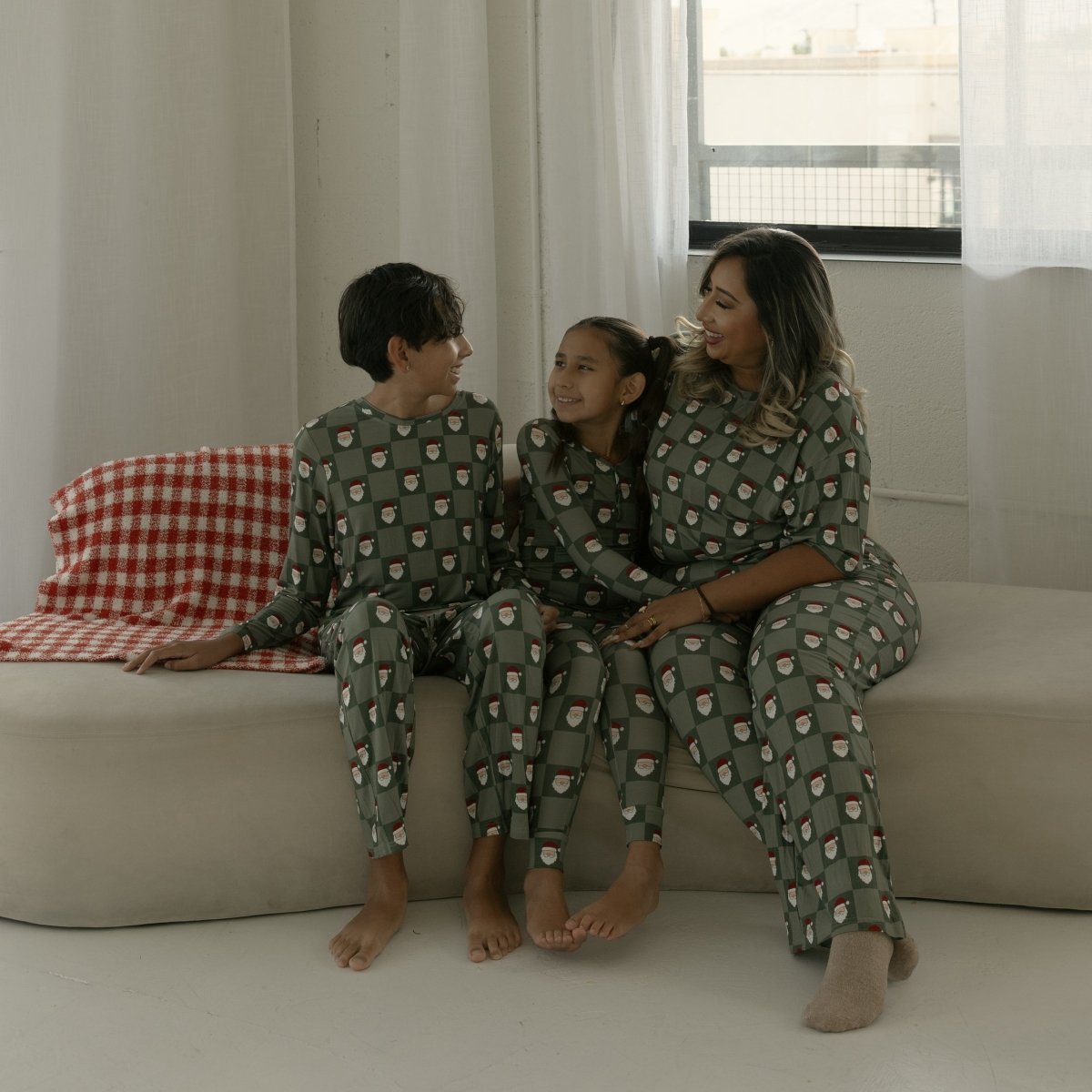 Family of three sitting on a couch wearing matching pajamas in a bright room.
