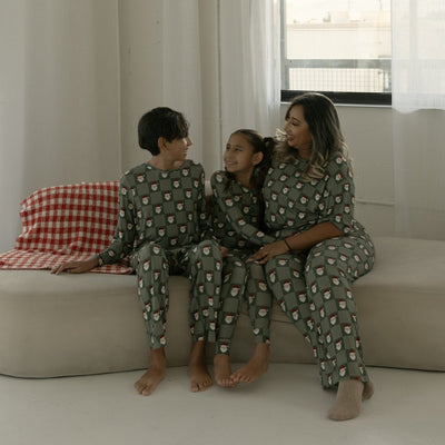 Family of three sitting on a couch wearing matching pajamas in a bright room.