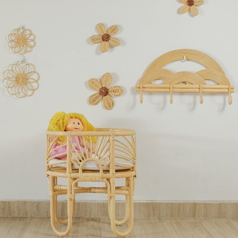 Rattan crib with a doll inside, surrounded by rattan flowers on a white wall.