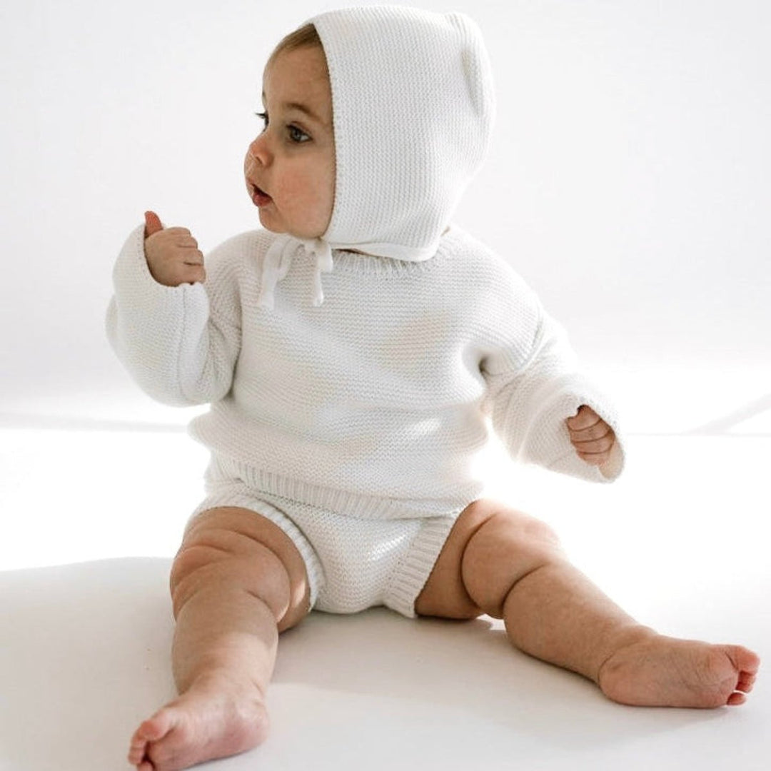 Baby wearing a white knitted outfit with a hood on a white background