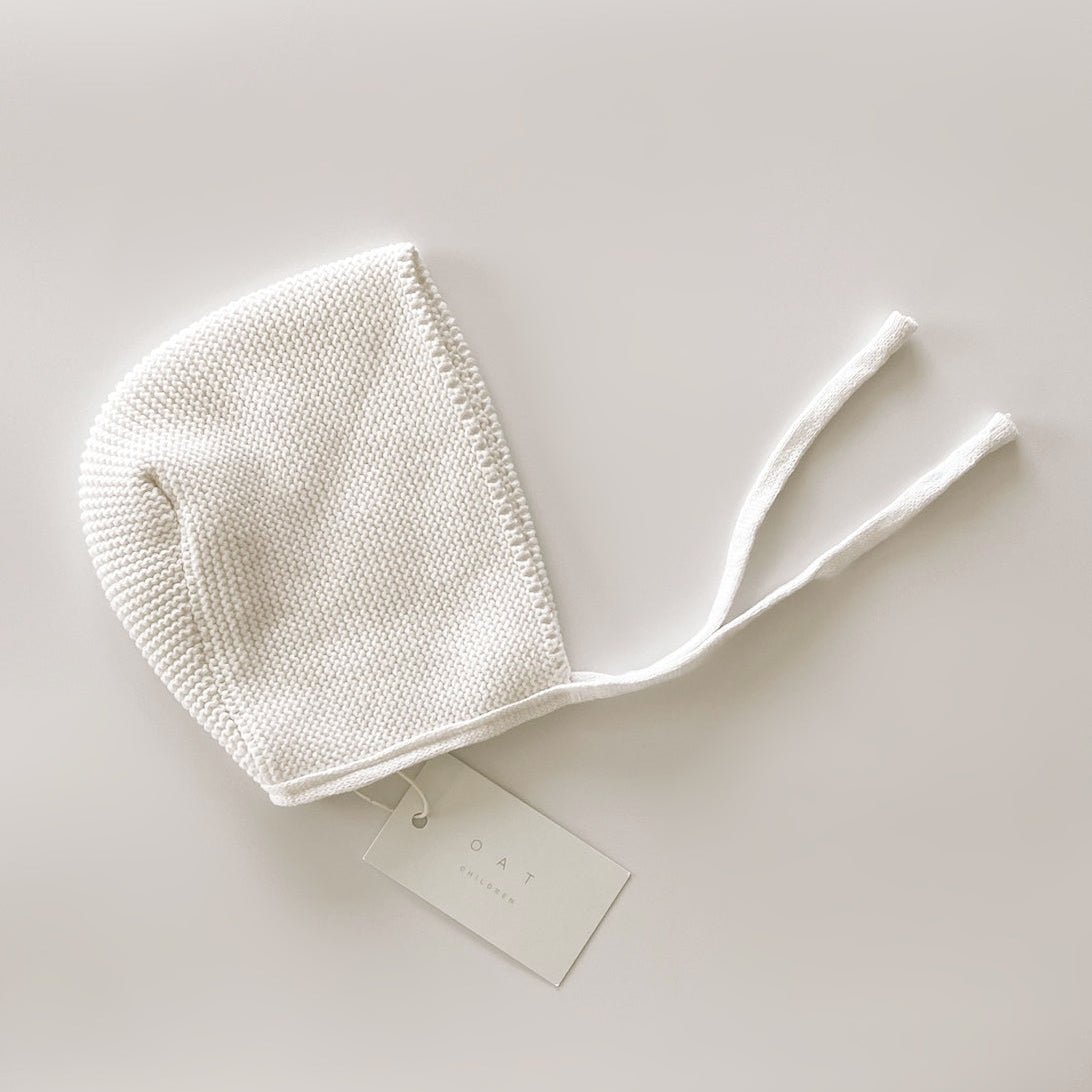 White knitted baby bonnet on a light gray background