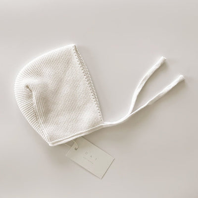 White knitted baby bonnet on a light gray background