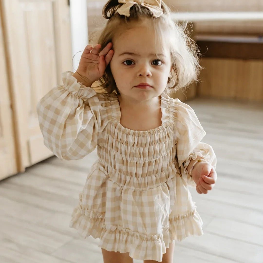 Young girl in a checkered dress standing on a wooden floor.