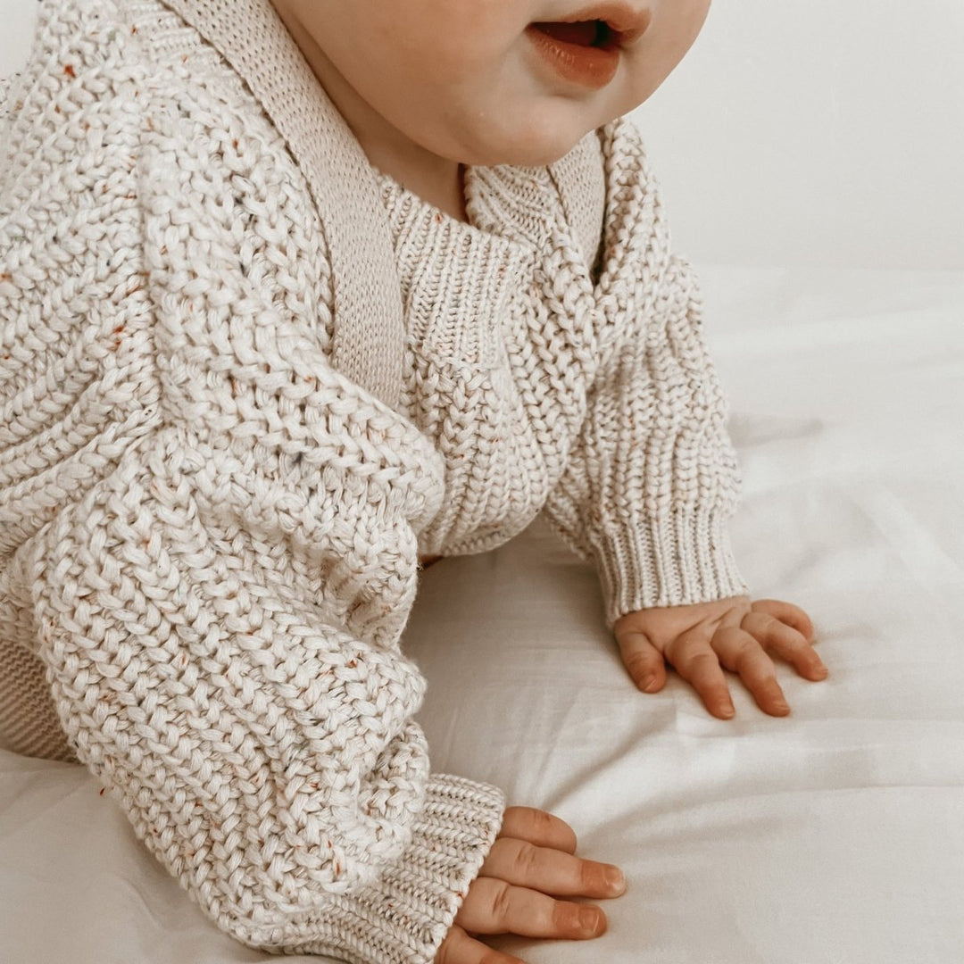 Baby wearing a beige knitted sweater on a soft surface